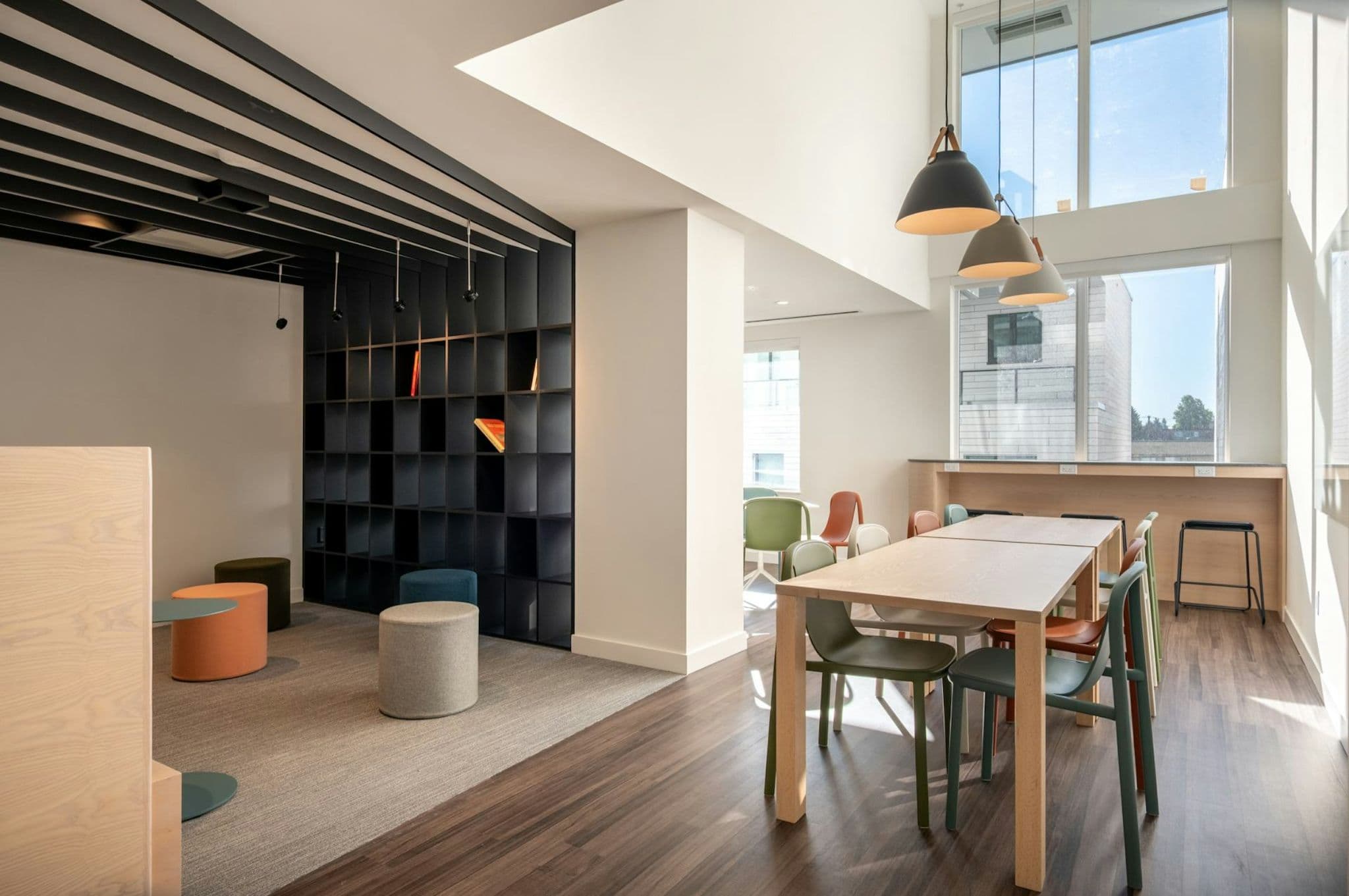 The Standard – Shared lounge/co-working space with a communal wood table, colorful chairs, built-in bookshelf, and floor-to-ceiling windows.