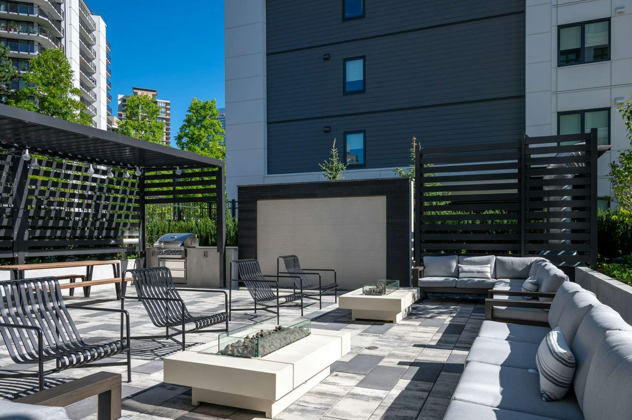 The Standard – Rooftop or courtyard patio with outdoor lounge seating, a fire pit table, a barbecue station, and city high-rises visible behind a privacy screen.