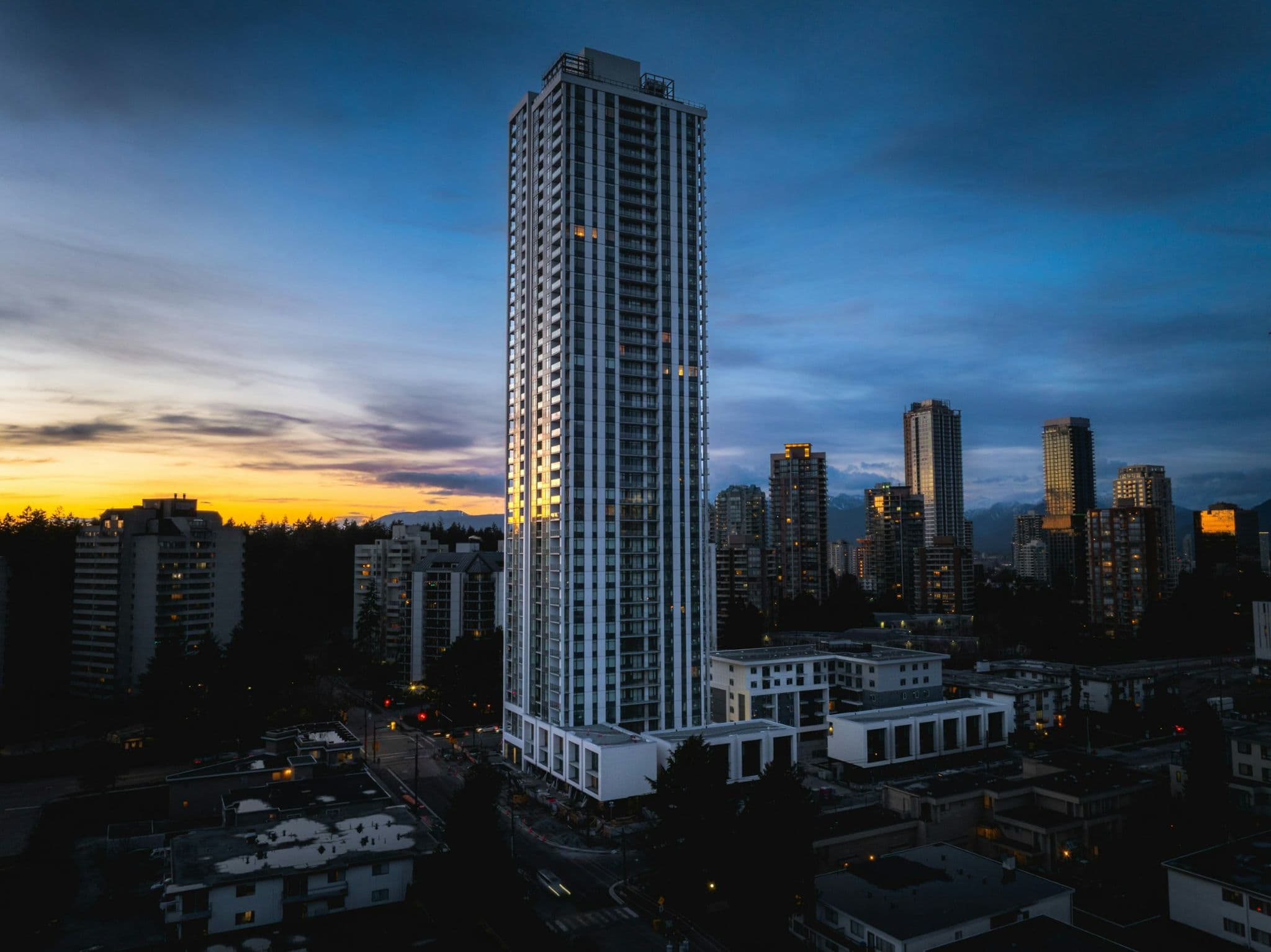 The Standard – Tall white high-rise residential tower photographed at dusk with a lit city skyline and mountains in the background.