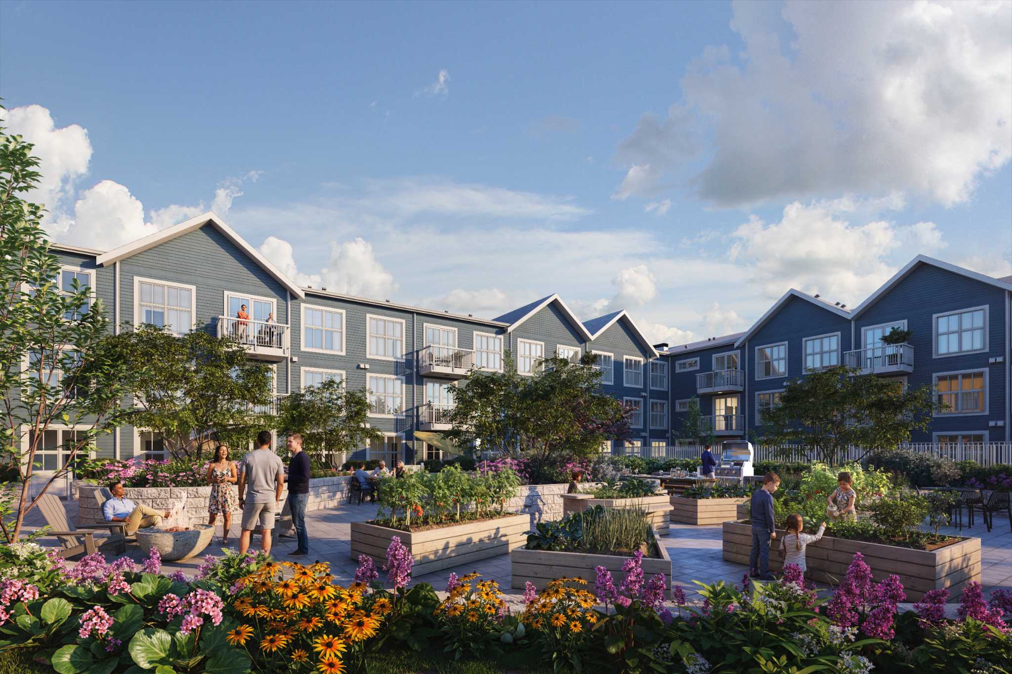 Market Commons – A paved outdoor residential courtyard features raised wooden garden planter boxes, lush flowerbeds, a fire pit, and BBQ grilling stations with people socializing. In the background, a multi-story blue-sided residential building with pitched gables and private balconies frames the sunny community space.