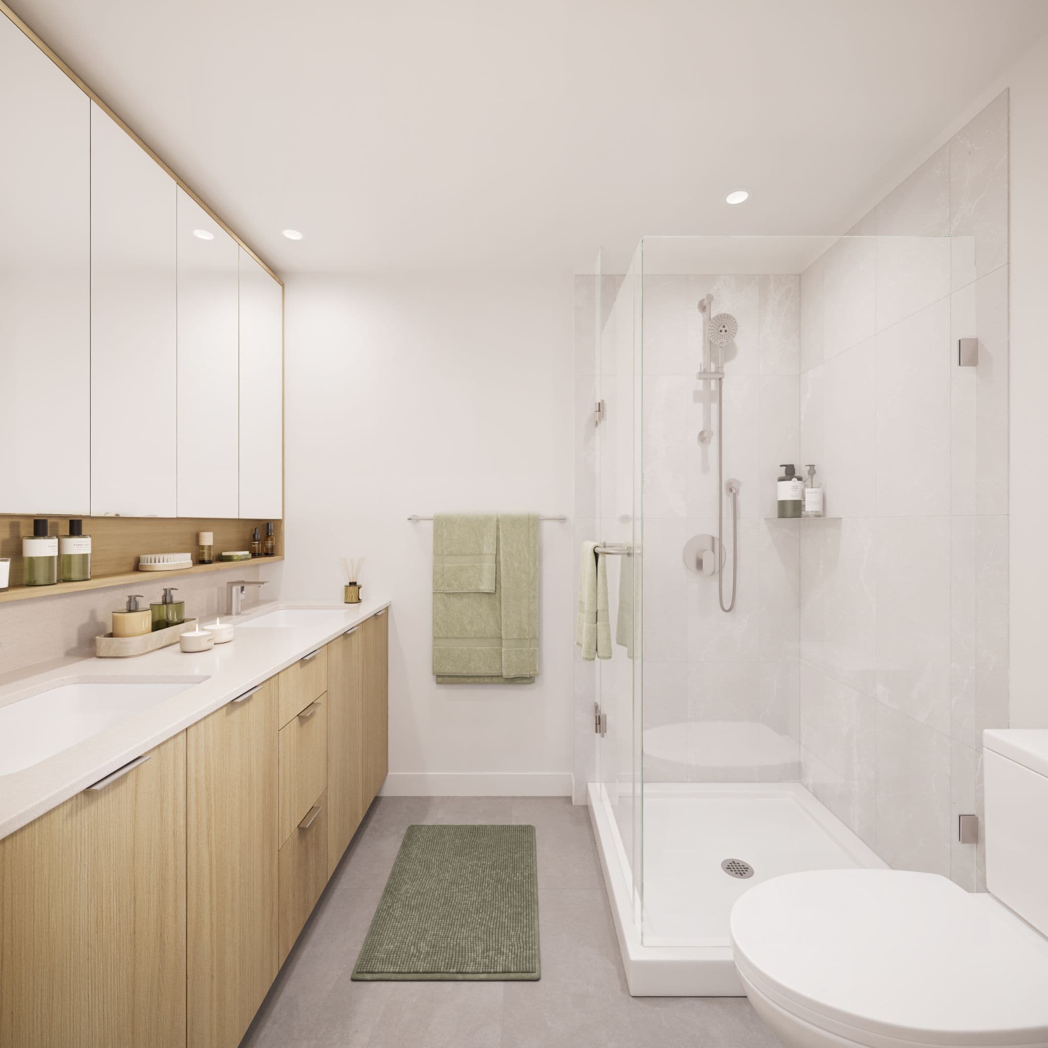 Market Commons – A modern, bright bathroom featuring a light wood double vanity with white countertops and mirrored upper cabinets. Across the grey-tiled floor sits a glass-enclosed walk-in shower with chrome fixtures and subtle marble-patterned wall tiles.