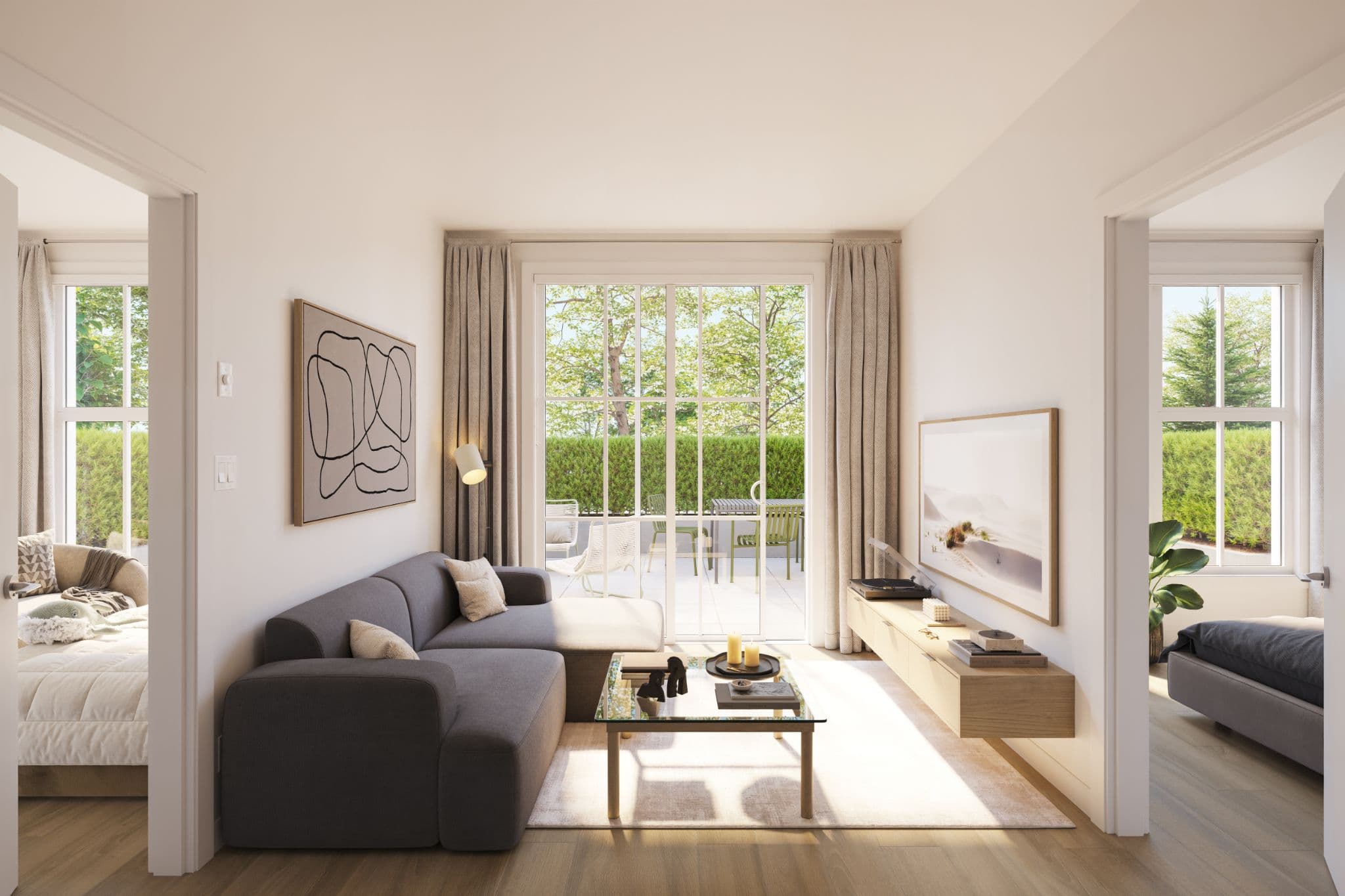 Market Commons – A bright, contemporary ground-floor living room features a charcoal sectional sofa, glass coffee table, and a floating wood media console facing large sliding glass patio doors. Sunlight pours in from the private outdoor patio lined with lush green hedges, framed by doorways offering glimpses into adjacent bedrooms.