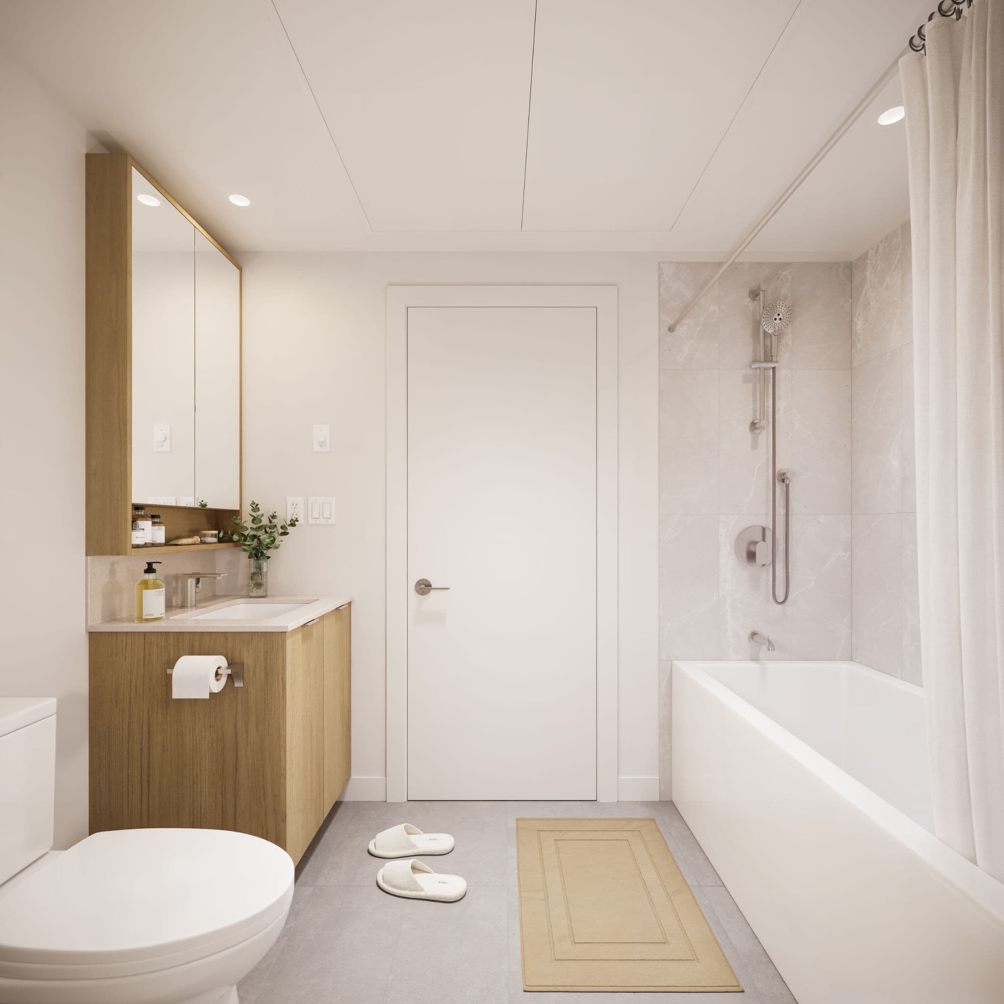Market Commons – A modern, minimalist bathroom features light wood cabinetry with an integrated medicine cabinet mirror, a white toilet, and a bathtub lined with subtle marble-patterned tiles and chrome fixtures. The space is finished with clean white walls, grey tiled flooring, a small beige bath mat, and recessed ceiling lighting for a bright, serene atmosphere.