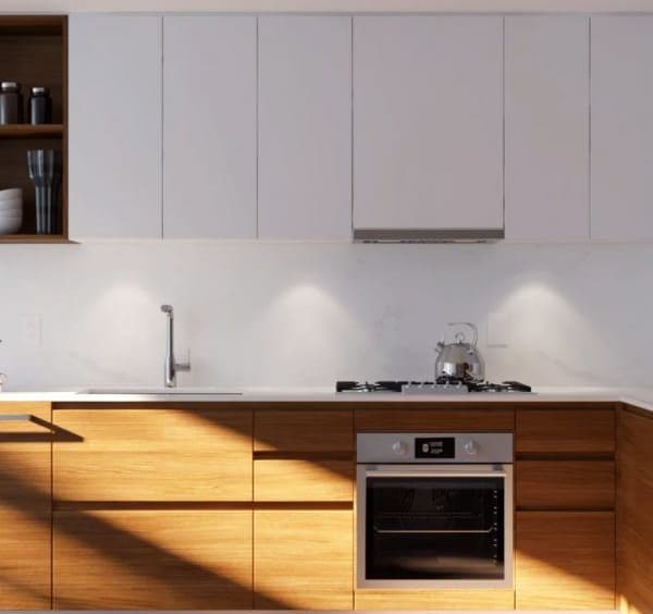 Wynwood Green – Close-up of a kitchen with white upper cabinets, wood lower cabinets, a gas cooktop, built-in oven, and a stainless kettle on the counter.