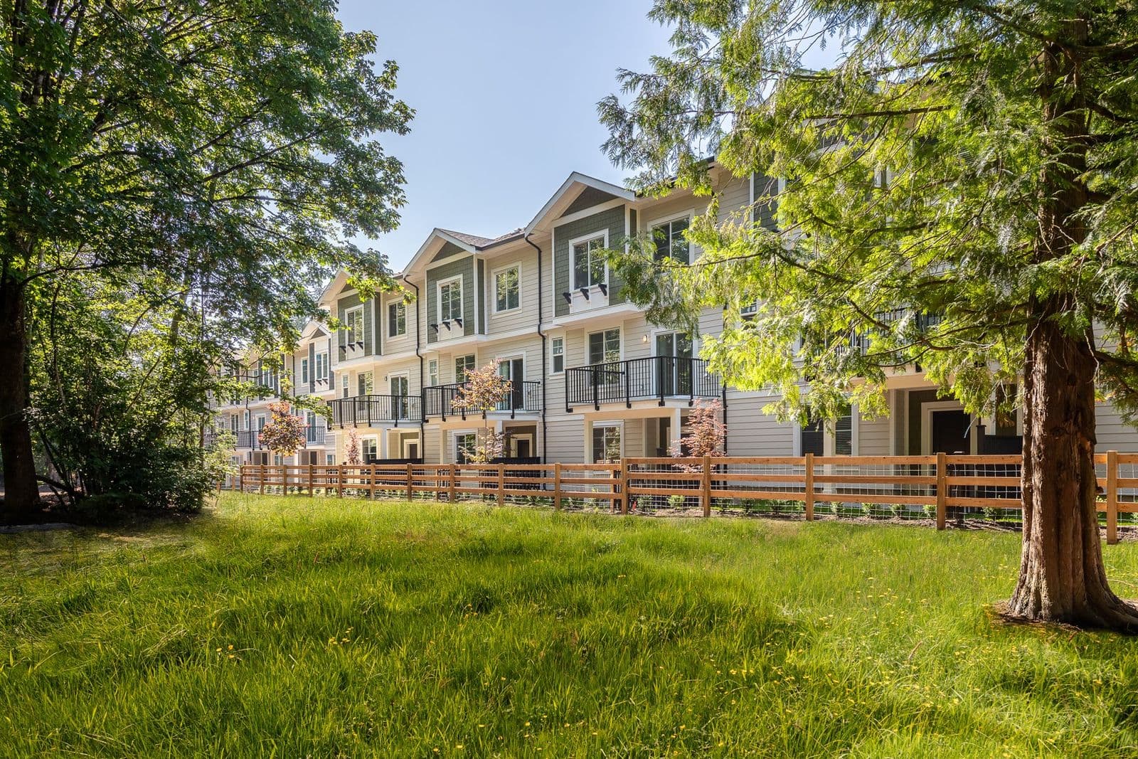 Griffon – Townhome building viewed across a grassy field with mature trees, a wood rail fence, and balconies visible on the upper floors.