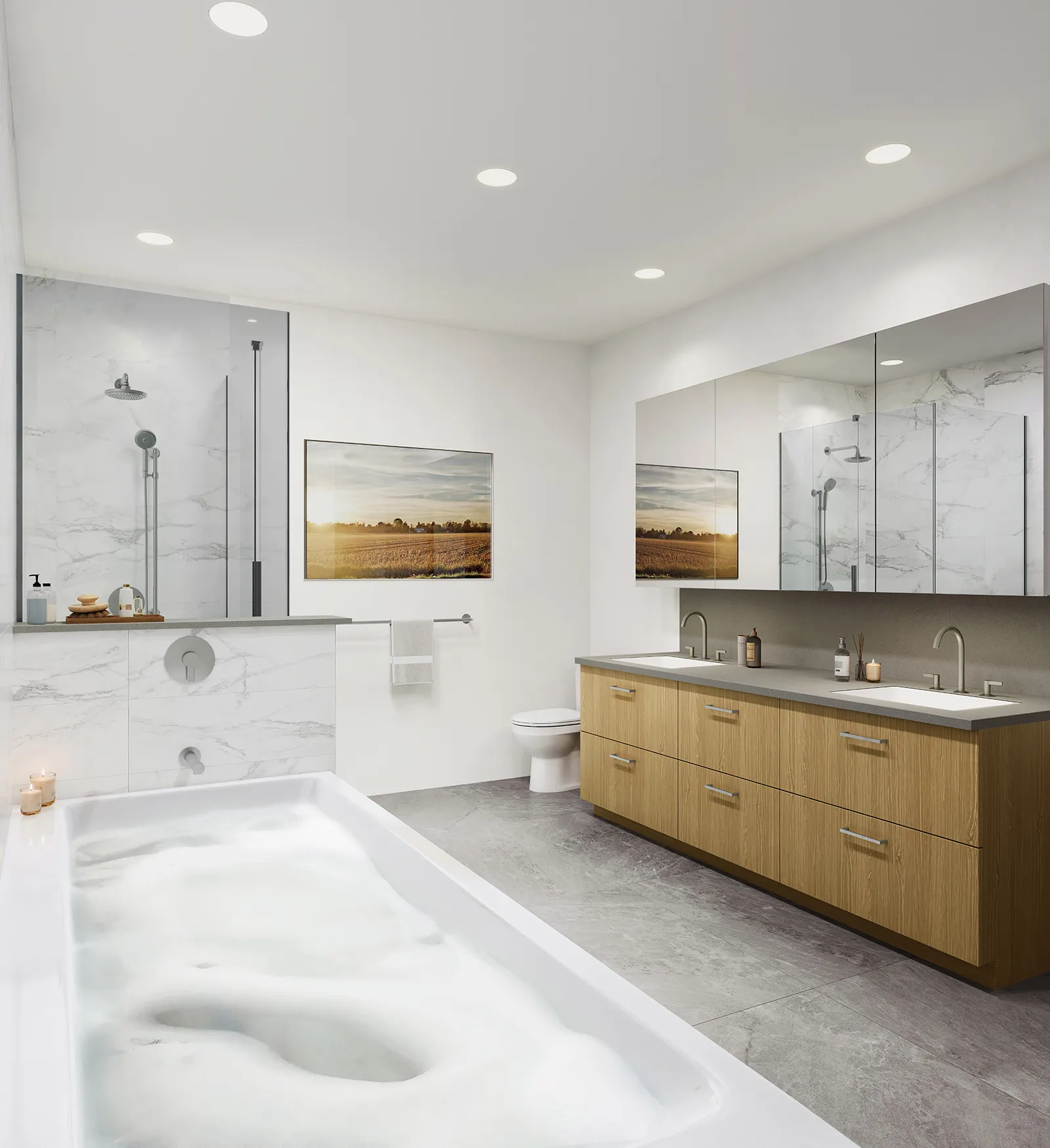 Bridge & Elliott – A modern, spacious bathroom features a large bubble-filled soaking tub in the foreground alongside a glass-enclosed shower with white marble tiling. A light wood double vanity with gray countertops and a wide mirrored medicine cabinet lines the right wall, set against gray floor tiles and recessed ceiling lighting.