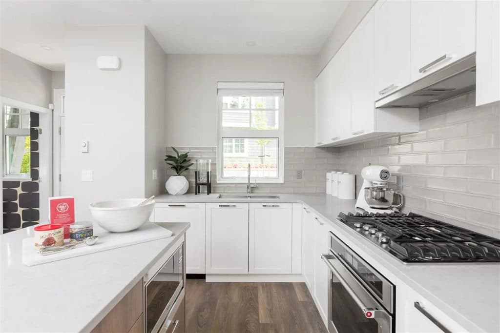 Forester at Burke Mountain Towns – White kitchen with subway tile backsplash, gas range, stainless appliances, and a window over the sink.