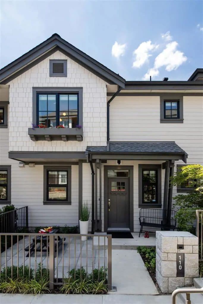 Forester at Burke Mountain Towns – Close-up of a townhome front entrance with dark trim, shake siding, a balcony with flower boxes, and a covered porch.