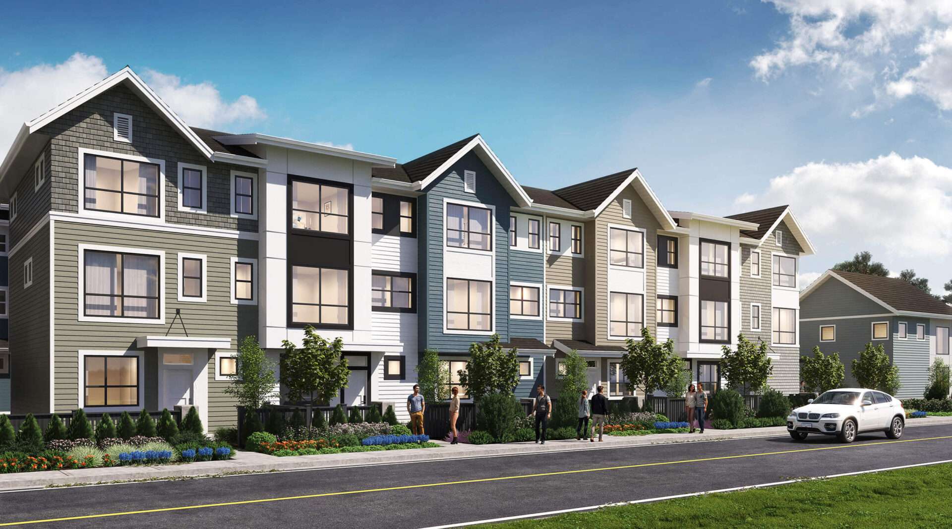 Silverbrook – A row of modern three-story townhomes features a mix of grey, blue, beige, and white lap siding and dark gabled roofs under a bright daytime sky. Small landscaped gardens, young trees, and a paved sidewalk line the front of the complex, where several pedestrians stroll and a white SUV is parked along the street.