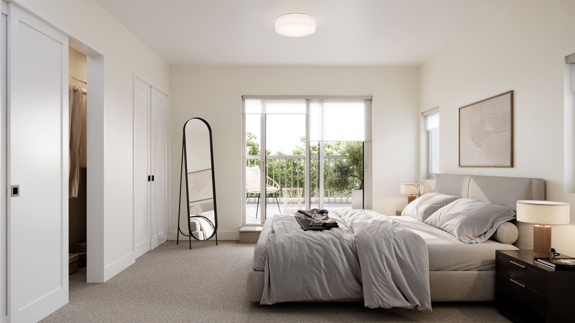 Oaklyn – A bedroom with a full-length mirror, a walk-in closet, a sliding glass door to a balcony, and a bed with a nightstand and lamp.