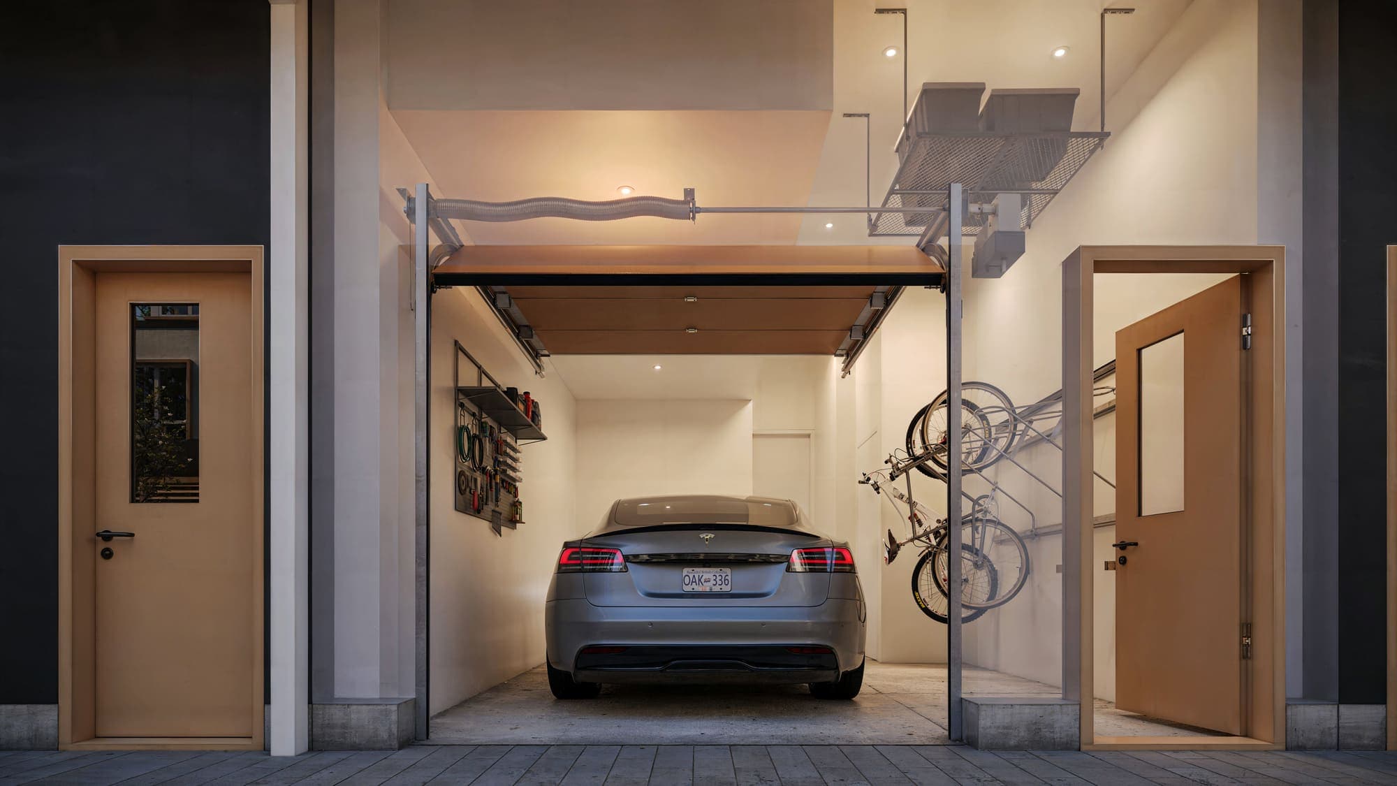 Oaklyn – A ground-level garage with a car parked inside, wall-mounted tool storage, hanging bike racks, and overhead storage shelving.