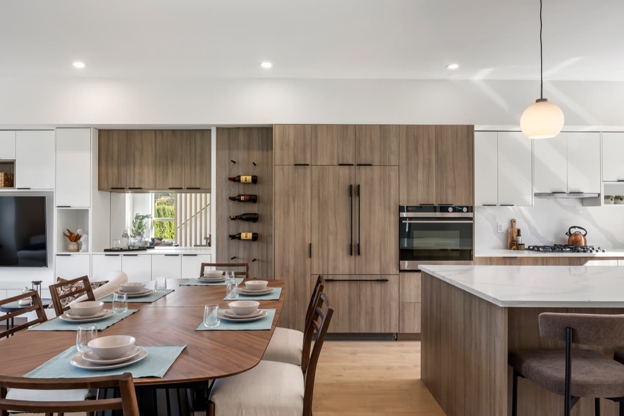 Signature – Wide view of the open kitchen and dining area showing the built-in refrigerator, wall oven, and island.