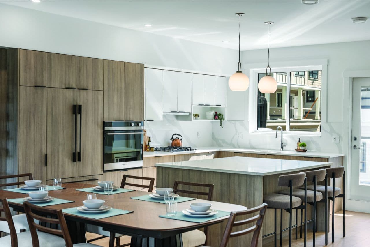 Signature – Kitchen and dining view with pendant lights and a window showing adjacent townhomes under construction.
