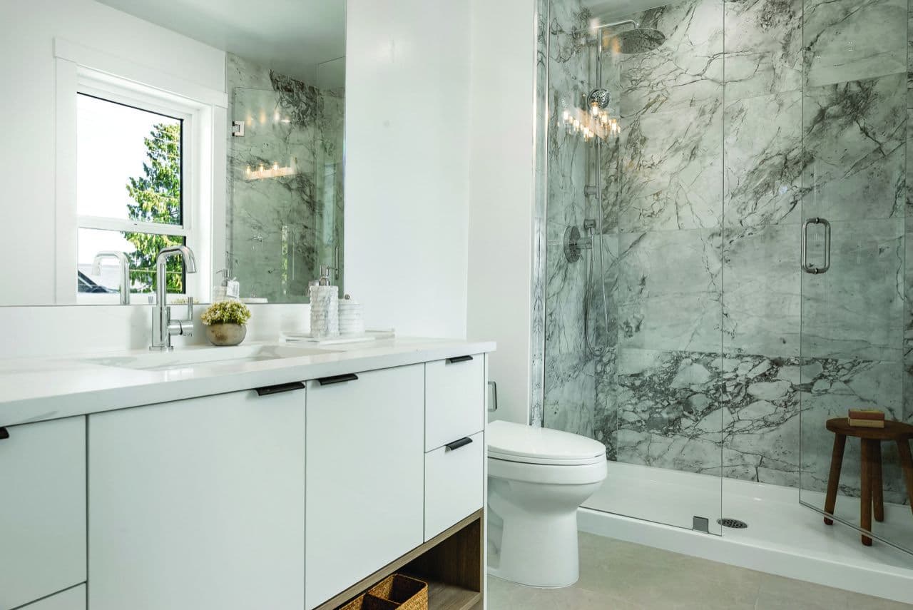 Signature – Bathroom with a marble-tiled glass-enclosed shower, toilet, and white vanity with black hardware.