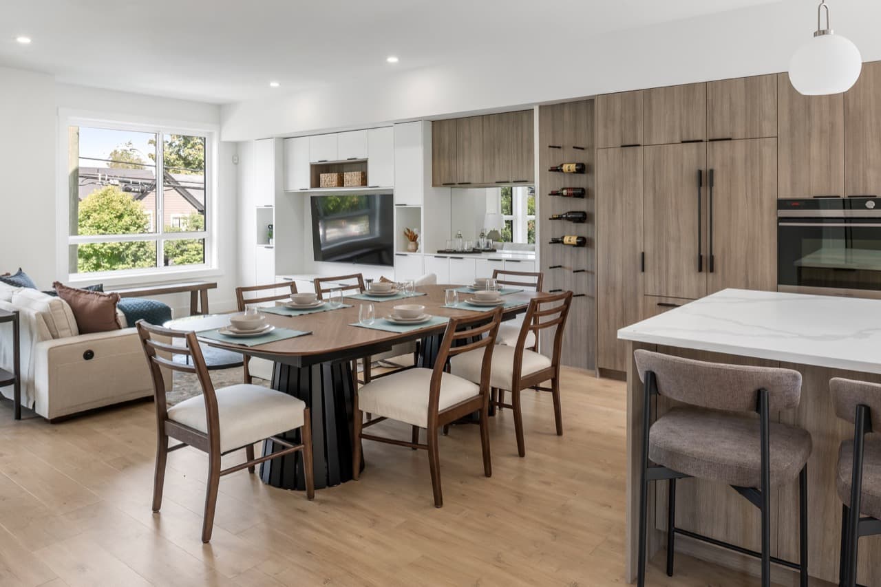Signature – Alternate wide-angle view of the open-plan living, dining, and kitchen area with a wood dining table set for a meal.