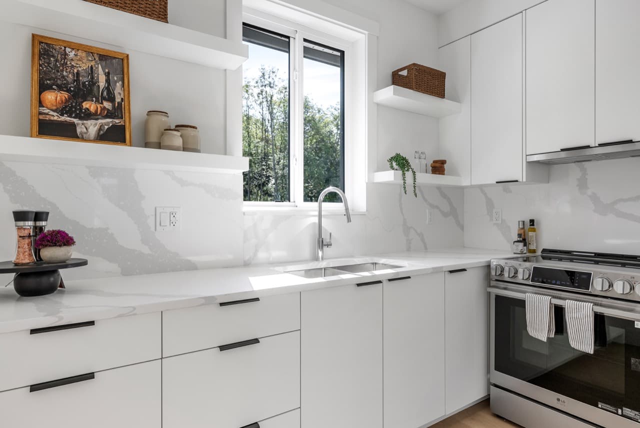 Signature – A different unit's white kitchen with a stainless steel range, open wood shelving, and marble backsplash.