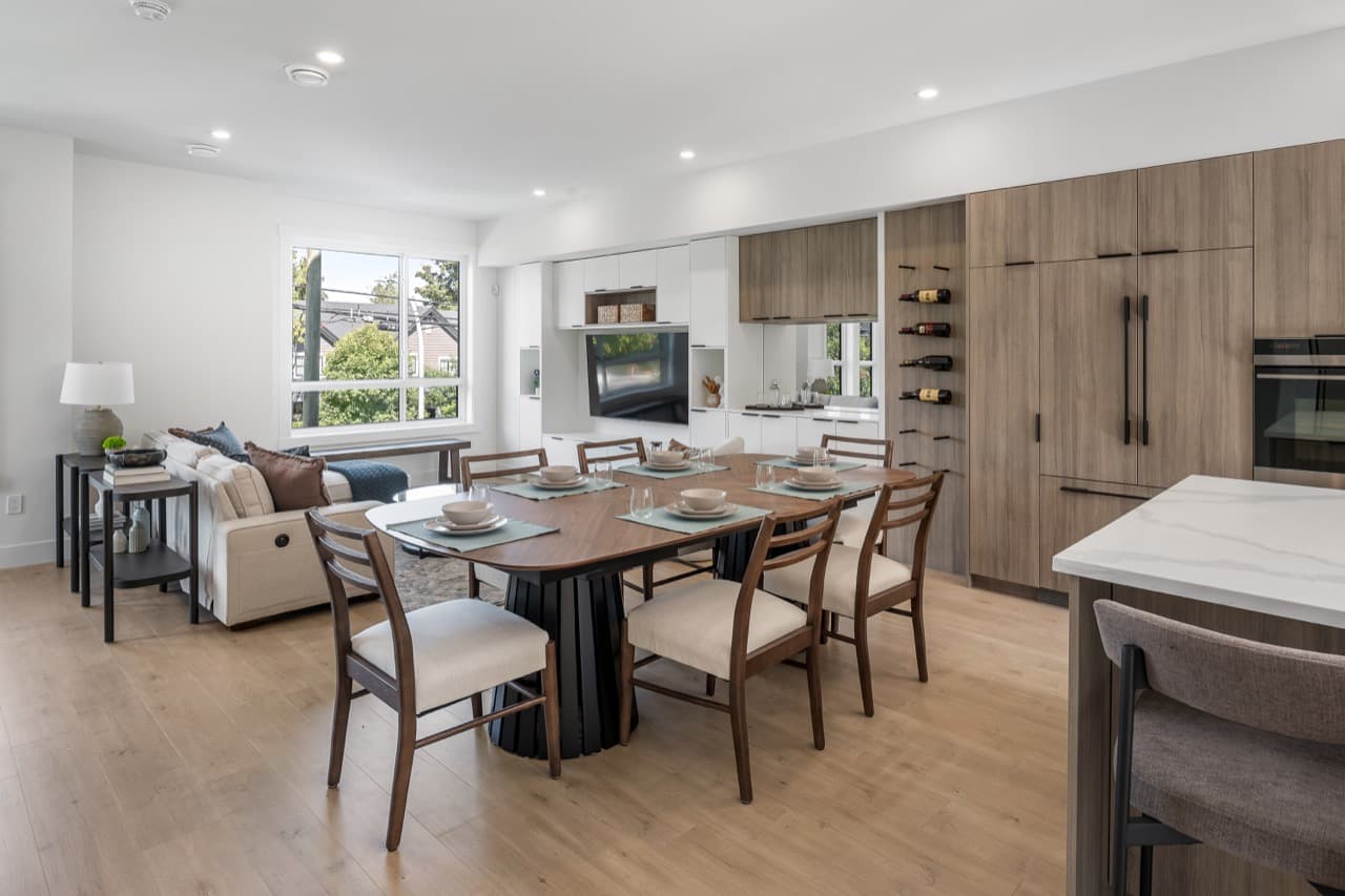 Signature – Open-concept dining and kitchen space with a wood dining table, upholstered chairs, wine rack cabinetry, and a built-in TV wall.