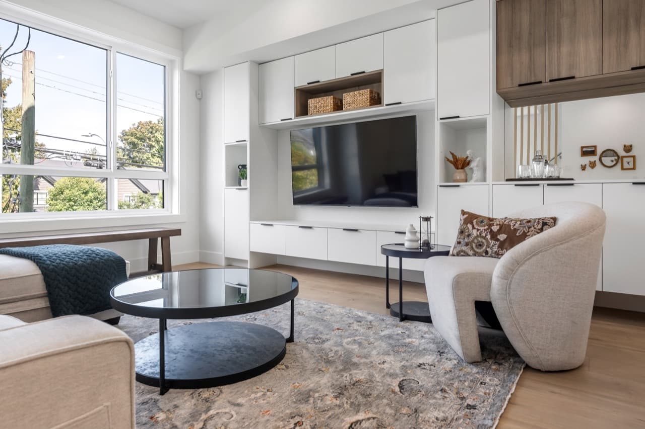 Signature – Living room with a built-in TV wall unit, round coffee tables, and a curved upholstered lounge chair.