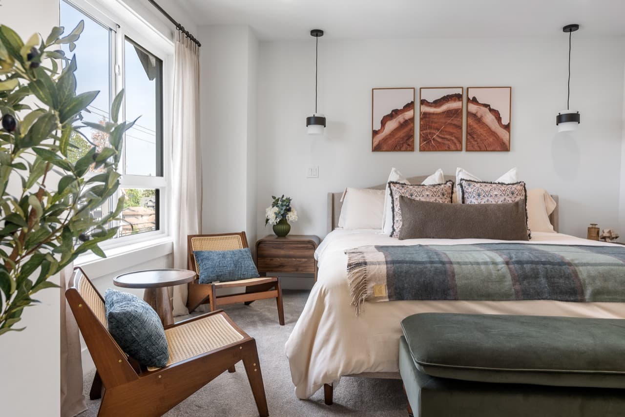 Signature – Primary bedroom with a king bed, patterned throw pillows, sitting chairs, and pendant lights flanking framed art.