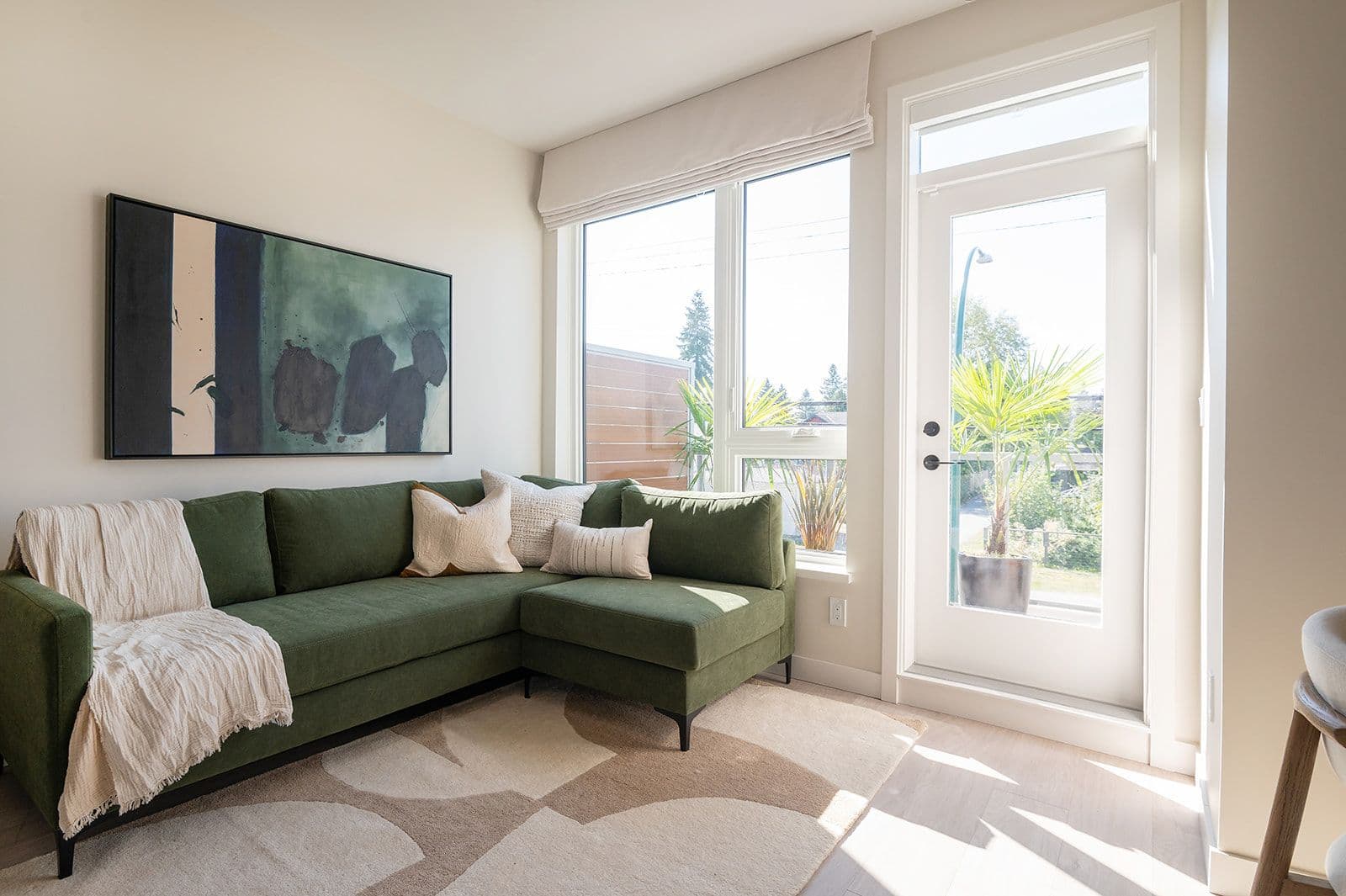 Sundays on Grant – A bright living room featuring a green sectional sofa, abstract wall art, and large windows leading to a patio door.