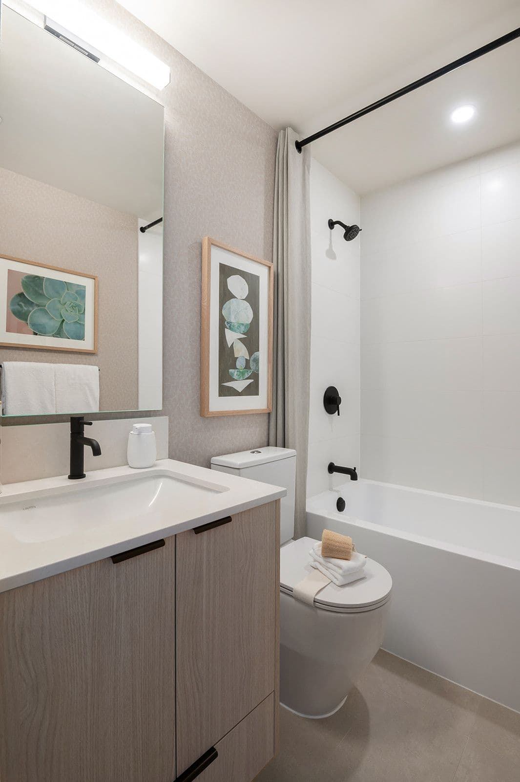 Sundays on Grant – A modern bathroom with a light wood vanity, black fixtures, a white bathtub, and framed art on the wall.