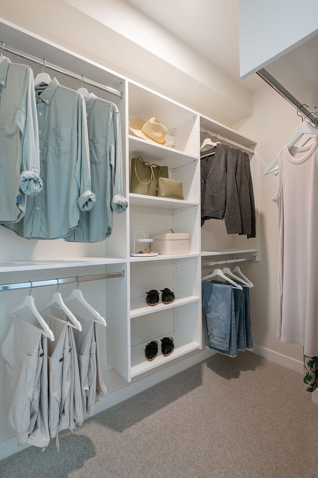 Sundays on Grant – A custom walk-in closet with white open shelving, hanging rods, clothes, shoes, and carpet flooring.