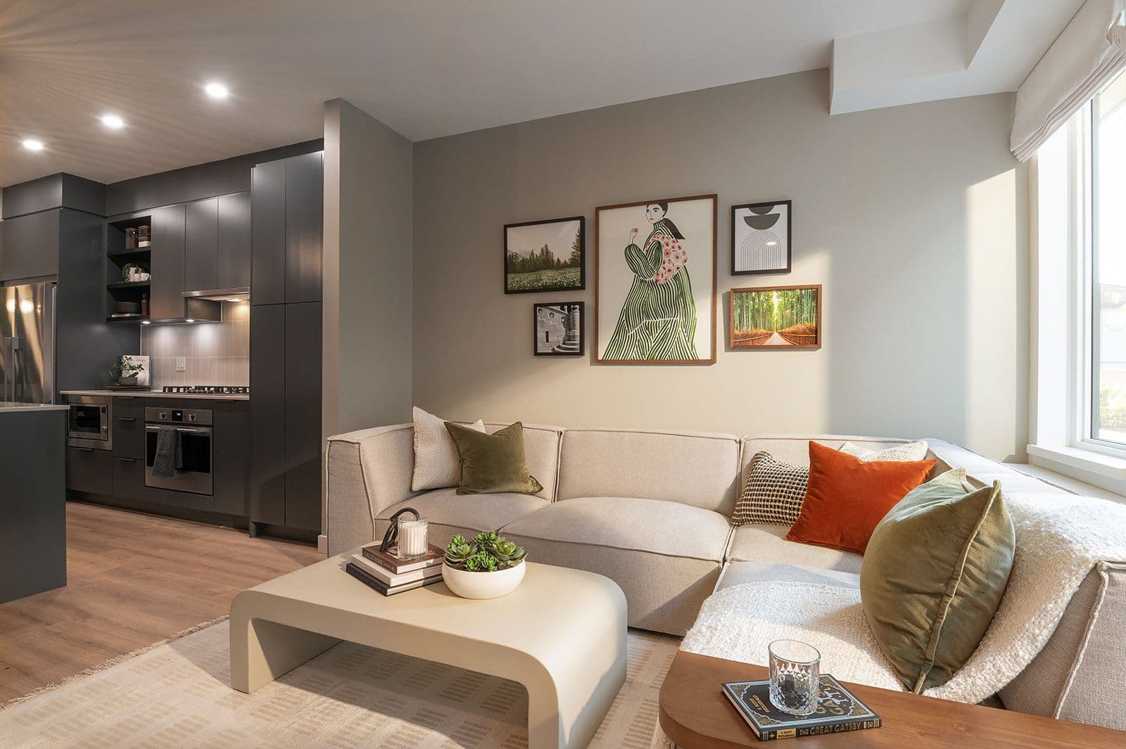 Sundays on Grant – A modern living space with a light beige sectional sofa, coffee table, gallery wall, and an adjacent dark-grey kitchen.