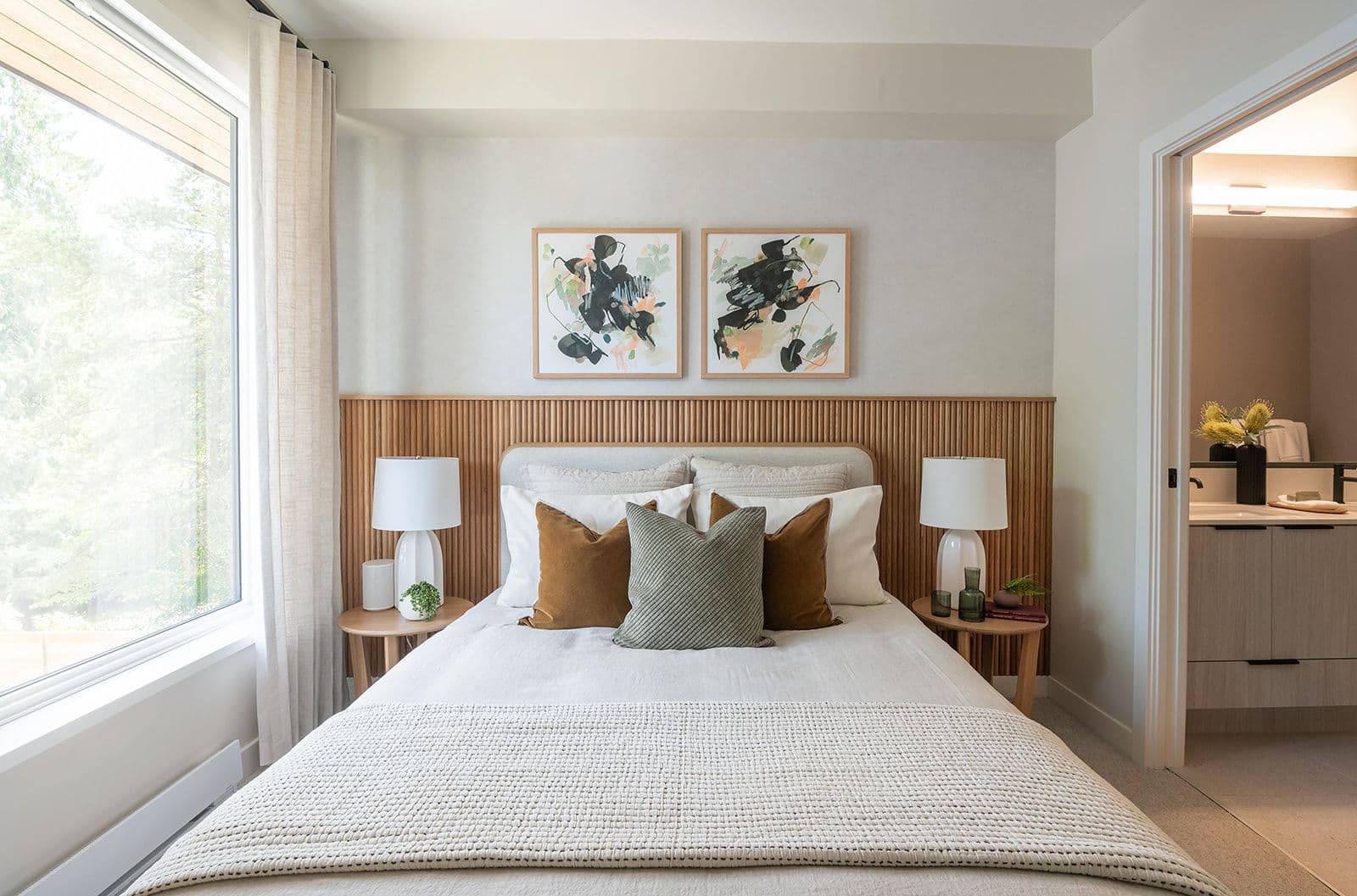 Sundays on Grant – A primary bedroom featuring a wood slat headboard, bedside lamps, large window, and access to an ensuite bathroom.