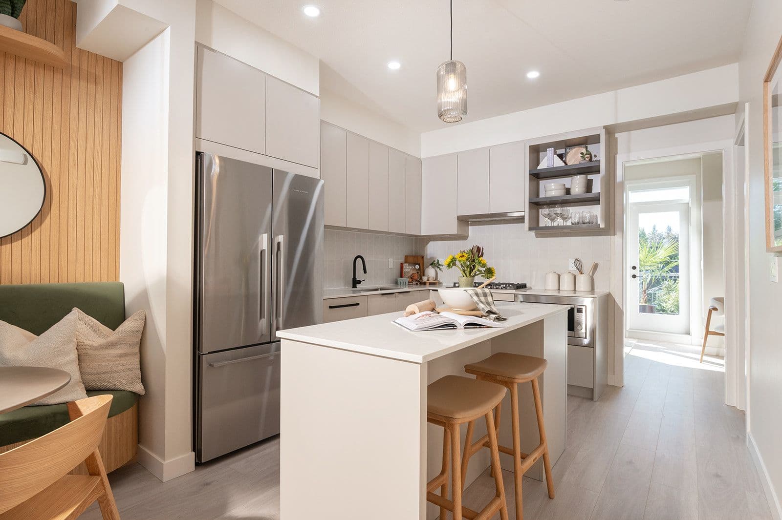 Sundays on Grant – A contemporary kitchen with light cabinetry, stainless steel refrigerator, kitchen island with seating stools, and adjacent banquette dining area.