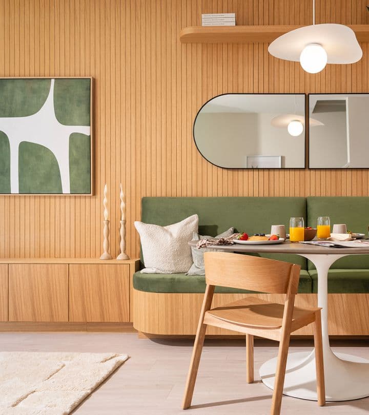 Sundays on Grant – Built-in dining nook featuring a green velvet bench seat, wooden slatted backdrop, pill-shaped mirrors, and round pedestal table.