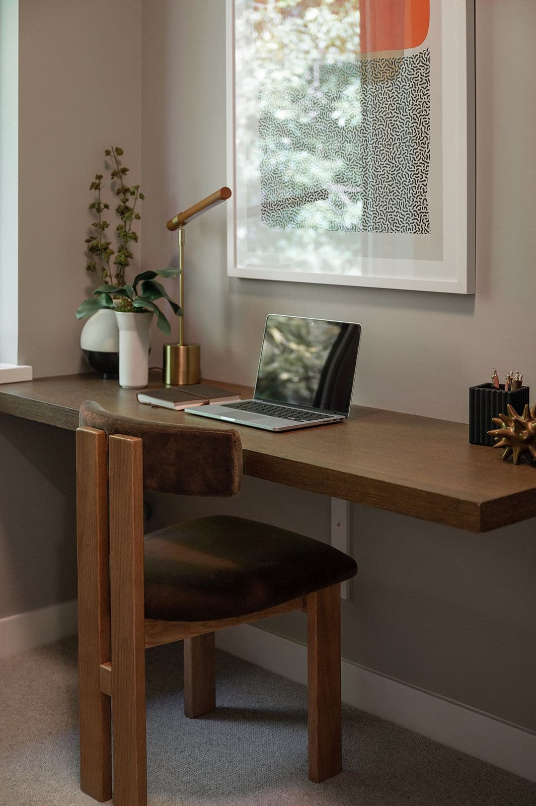 Sundays on Grant – A built-in home workspace nook with a floating wood desk, wooden chair, laptop, desk lamp, and framed wall art.