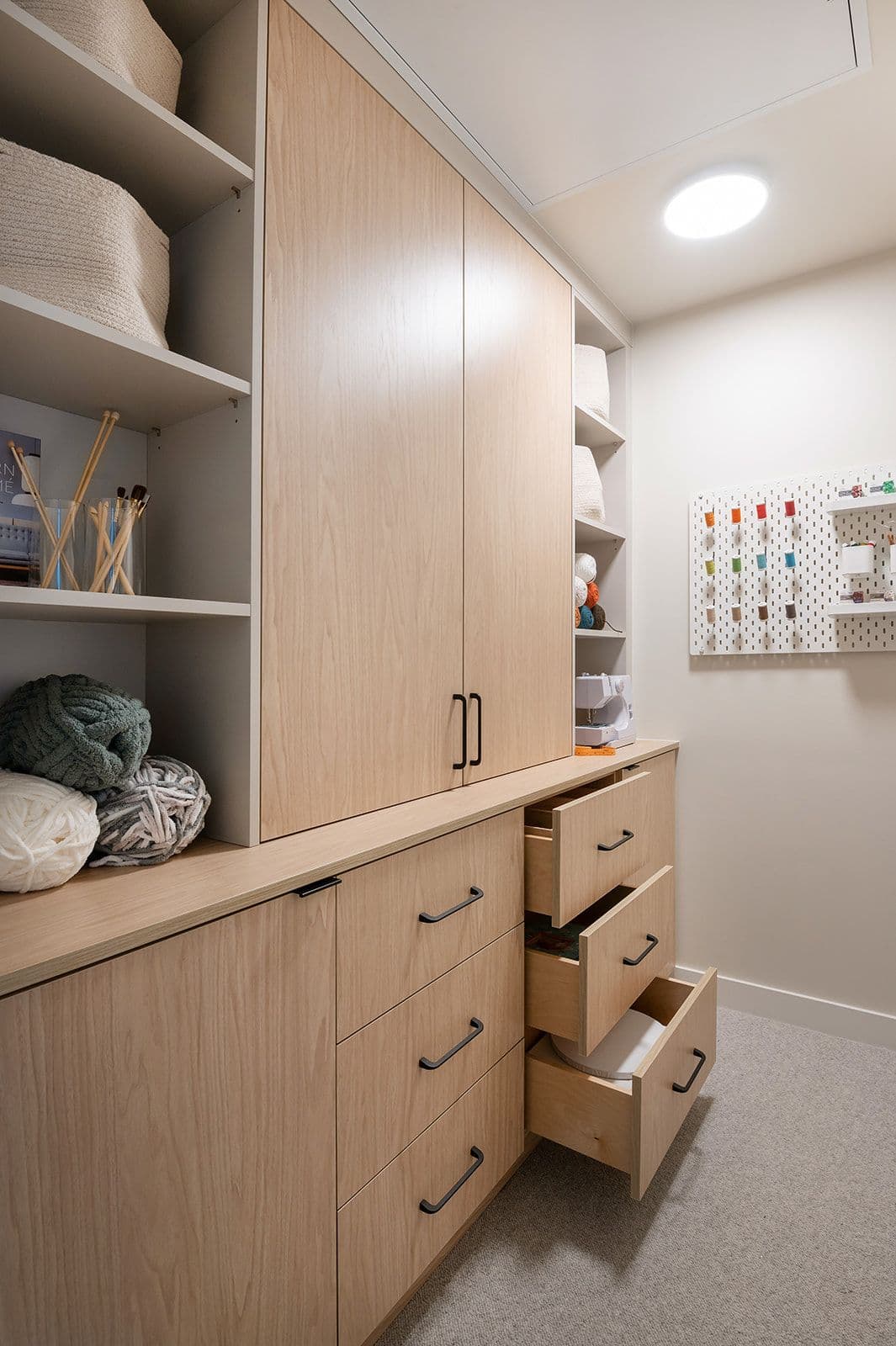 Sundays on Grant – Built-in storage and craft room cabinets with light wood drawers, shelving, and a wall pegboard for organizing supplies.