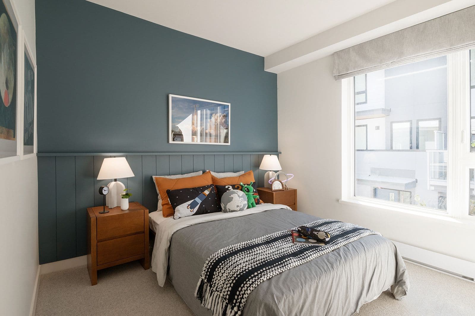 Sundays on Grant – A child's space-themed bedroom with a teal accent wall, wooden nightstands, space pillows, and a large window.