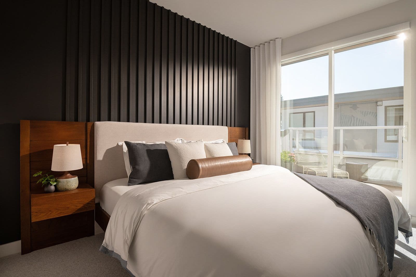 Sundays on Grant – Modern bedroom featuring a dark wood slat headboard feature wall, sliding glass doors to a balcony, and warm lighting.