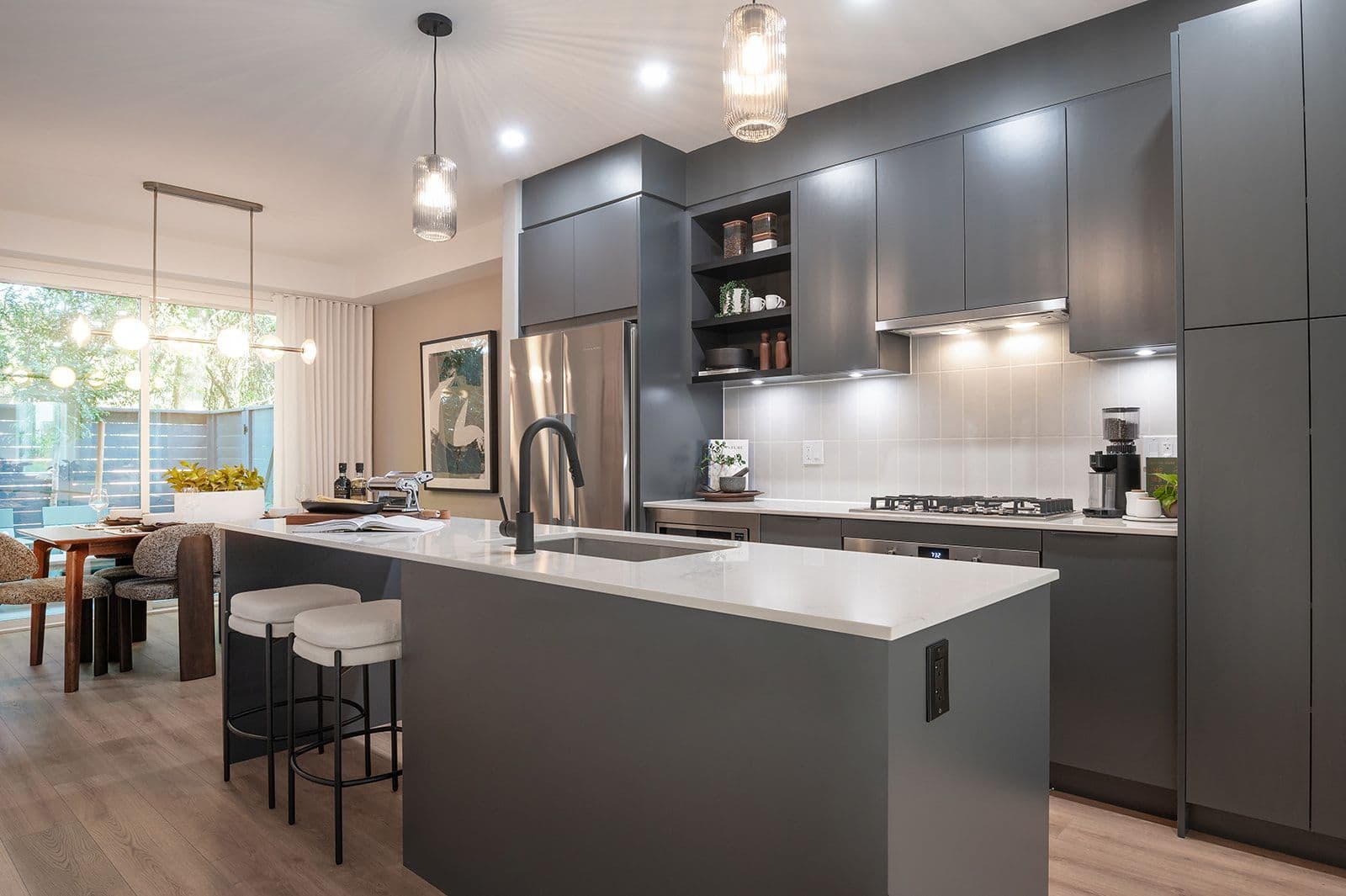 Sundays on Grant – Modern dark grey kitchen with a quartz island, sink, bar seating, gas range, and view into the adjacent dining room.