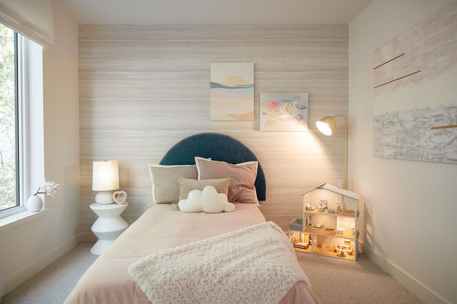 Sundays on Grant – A child's bedroom with an arched navy velvet headboard, subtle striped wallpaper wall, dollhouse, and soft ambient lighting.