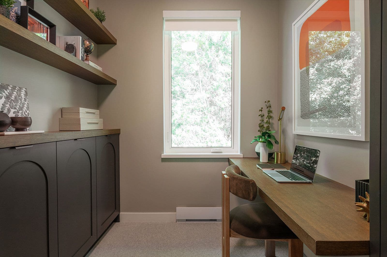 Sundays on Grant – Dedicated home office room featuring built-in cabinetry, floating wooden shelves, desk with laptop, and a window with tree views.