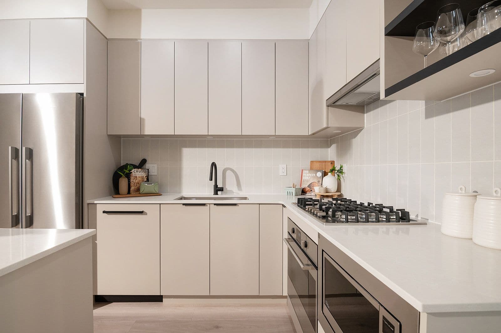 Sundays on Grant – Modern L-shaped kitchen featuring light beige flat-panel cabinets, gas cooktop, black faucet, and white tile backsplash.
