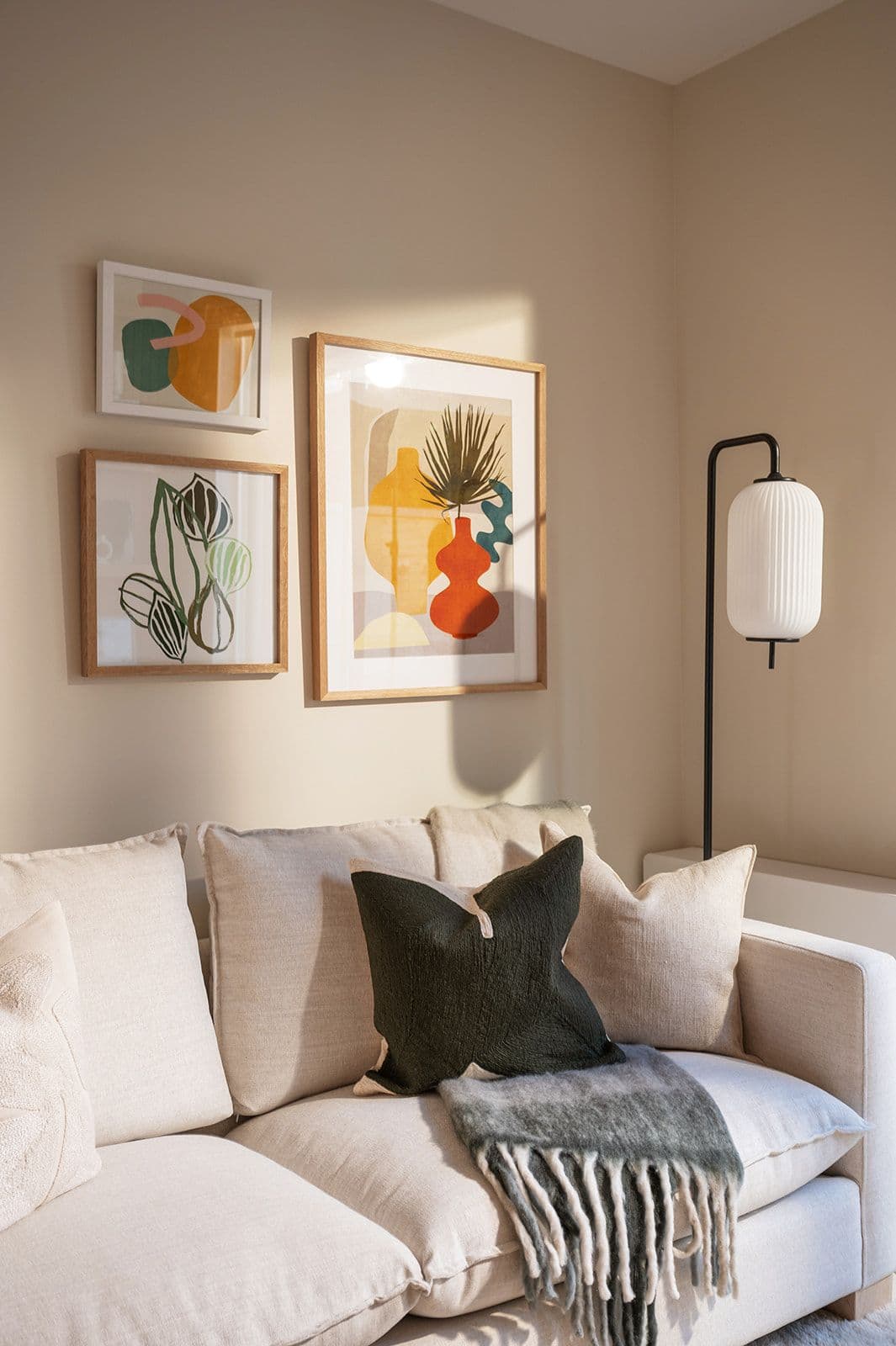 Sundays on Grant – Cozy living room corner showing a beige fabric couch with accent pillows, floor lamp, and wall gallery art.