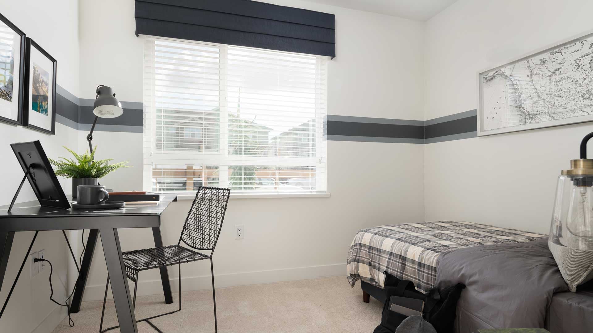 Aston – A study/bedroom with a black desk and chair, a map on the wall, and a plaid-covered daybed near a window.