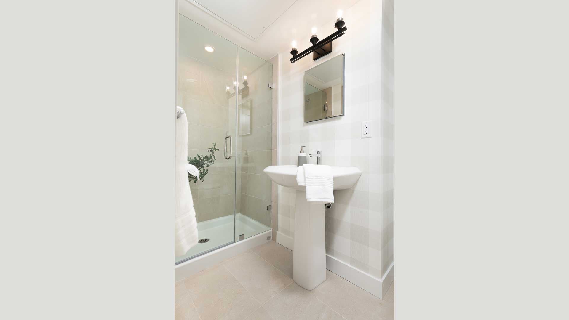 Aston – Bathroom with a glass-enclosed shower, a pedestal sink, and checkered wallpaper on the walls.