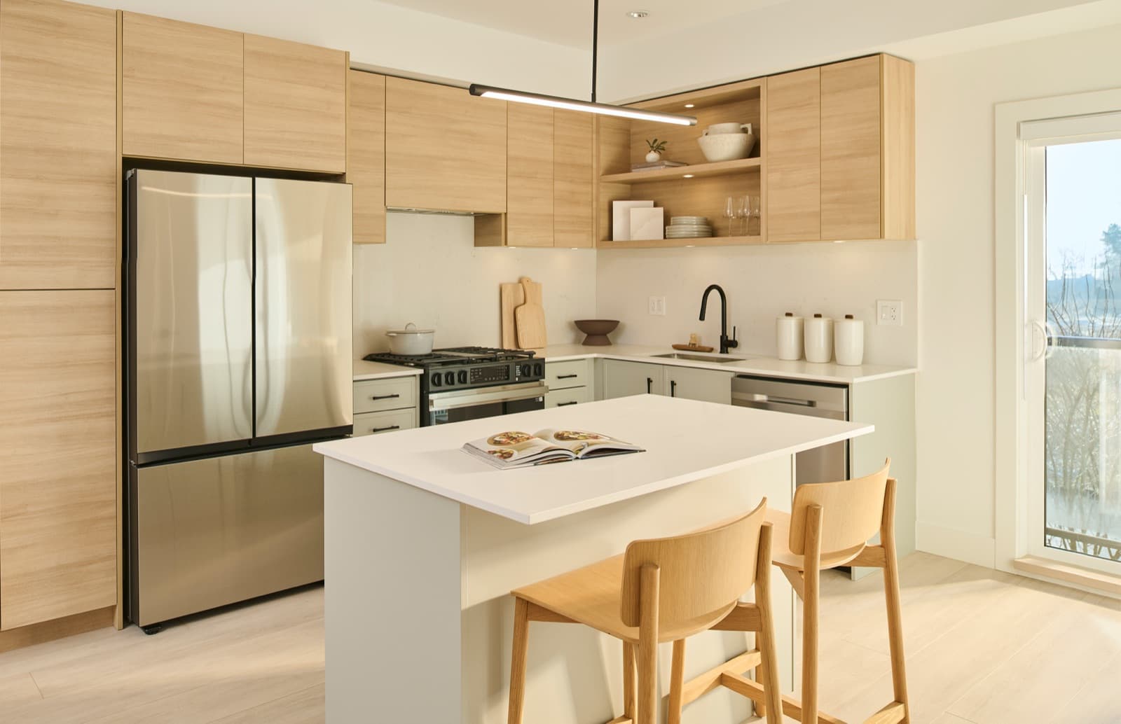 Addition Living – Kitchen with light wood cabinetry, open shelving, a stainless fridge, gas range, and a white-topped island with two wood bar stools.