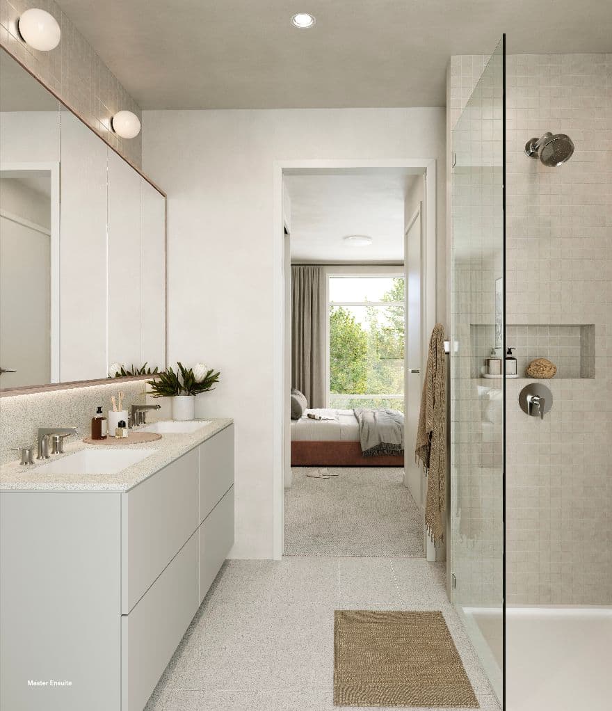 Rowen W47th – Master ensuite bathroom with a double vanity, terrazzo-look flooring, a glass-enclosed shower, and a view through to a bedroom with a window overlooking trees.