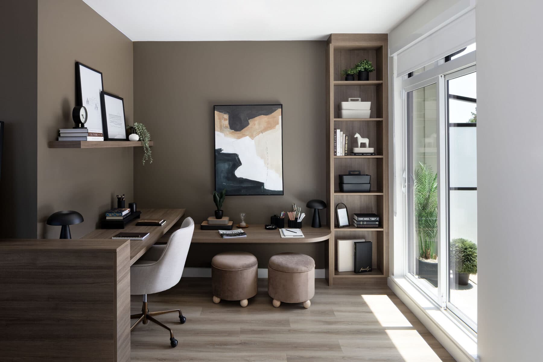 Rindall – Home office nook with a built-in desk, bookshelf with decor, and two round ottomans.