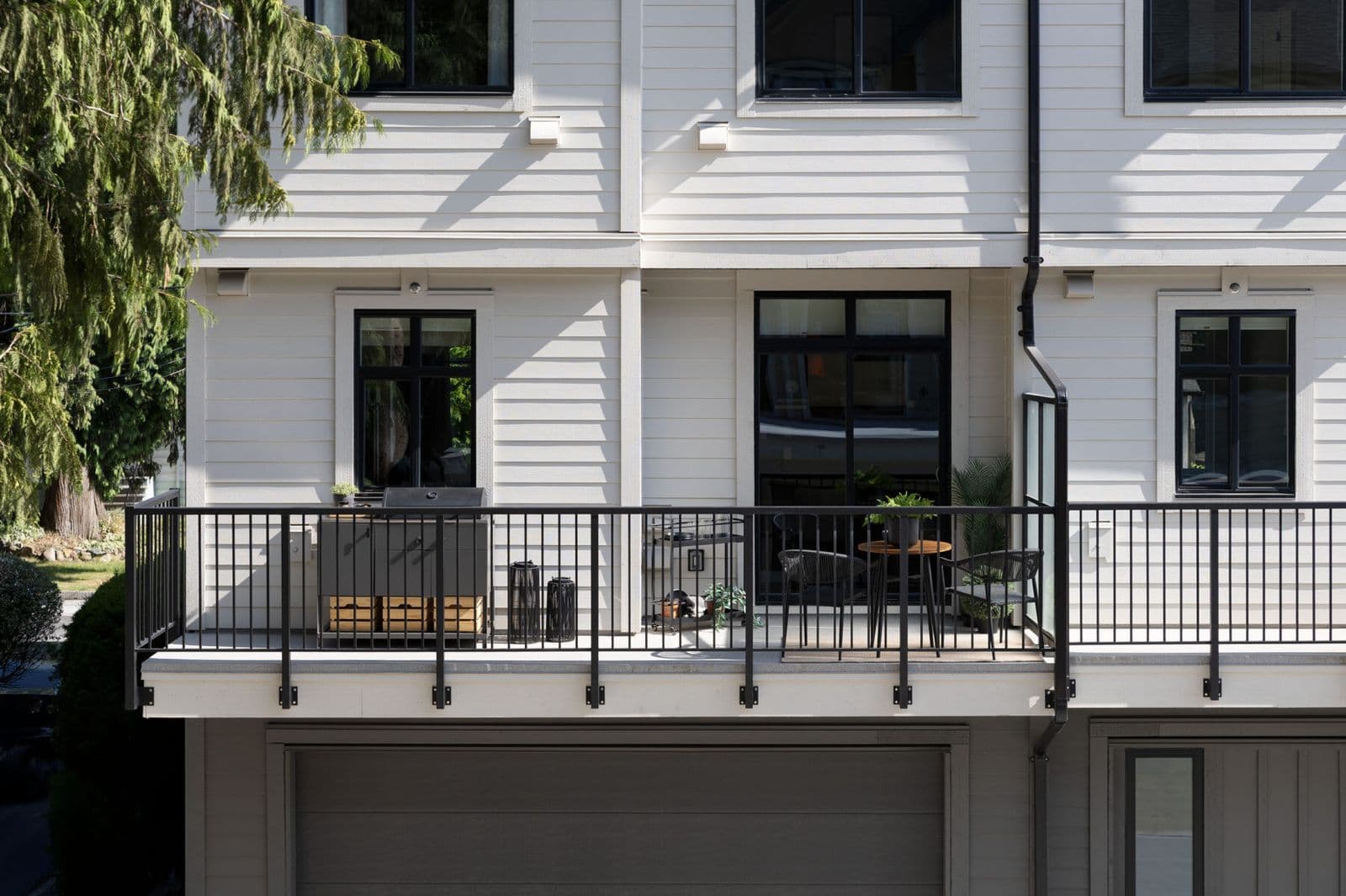 Rindall – Close-up of a private balcony with a barbecue, patio furniture, and black railings on the building's white siding.