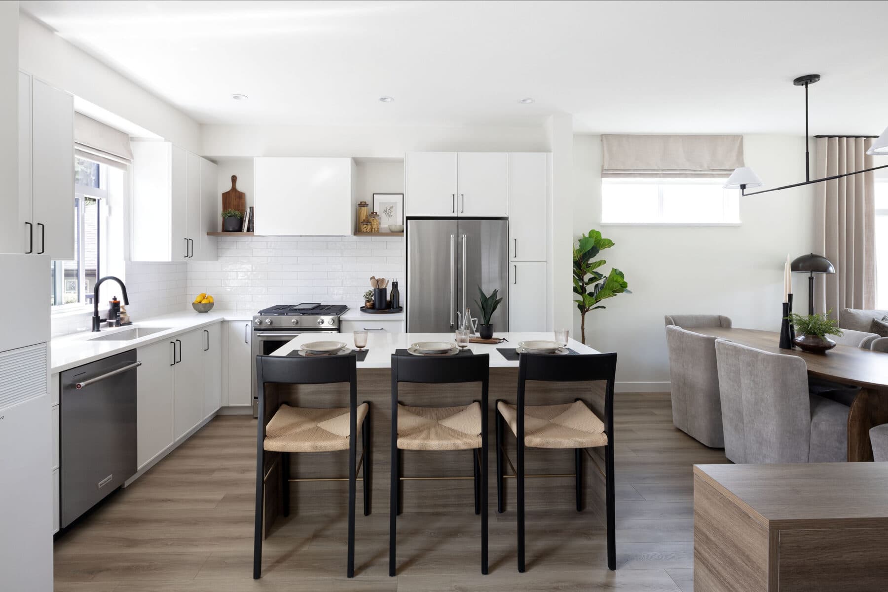 Rindall – Kitchen with white cabinetry, stainless-steel fridge, and a wood-look island with black bar stools, opening to a dining area.