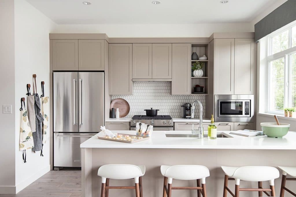 Baycrest West Condos – Kitchen with taupe cabinetry, a hexagon tile backsplash, stainless fridge and range, and a white island with round-top bar stools.