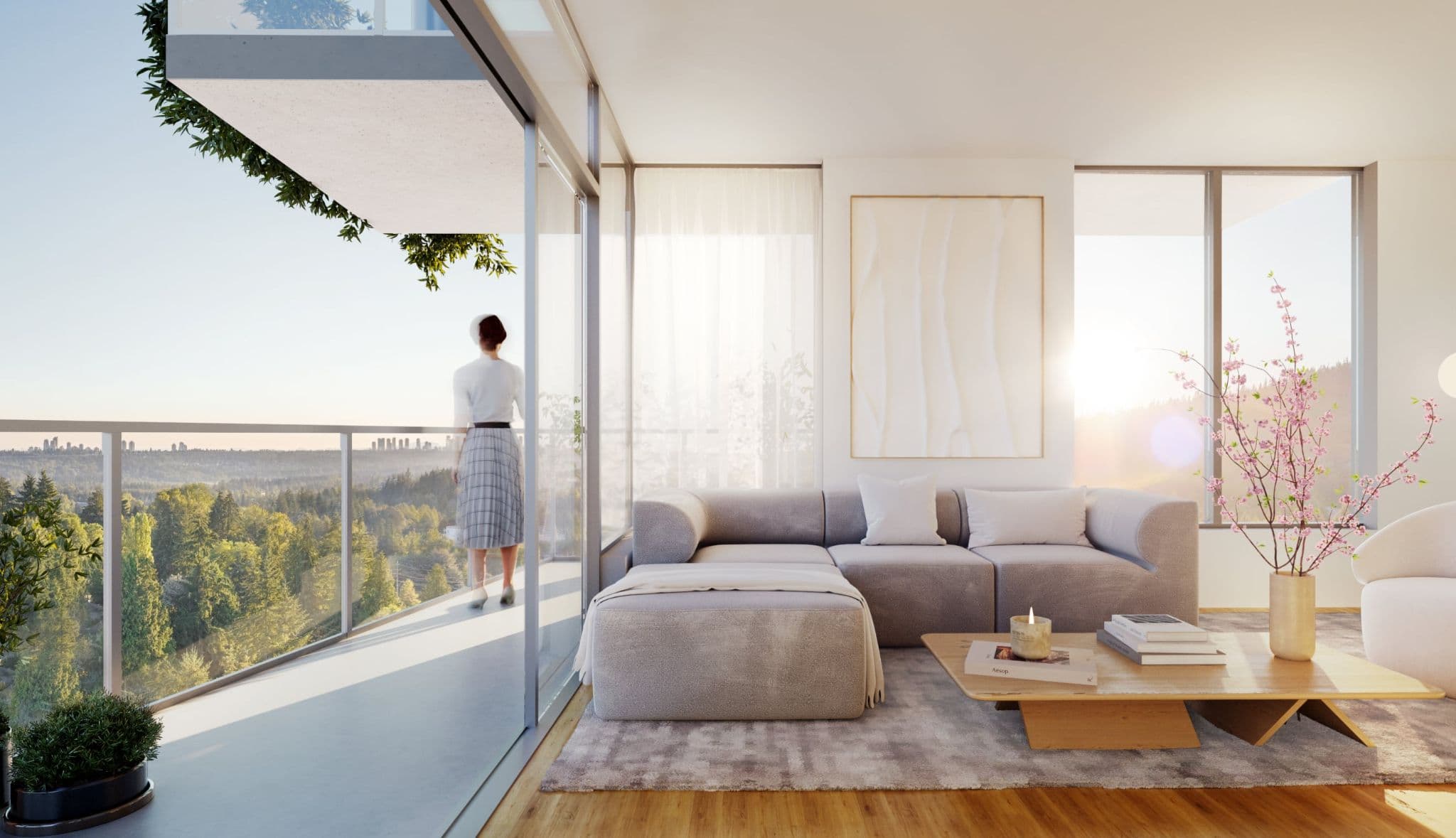 Gardena – A furnished living room with a grey sectional sofa, coffee table, and framed art, with a woman standing on the adjoining balcony overlooking forested hills and a city skyline.