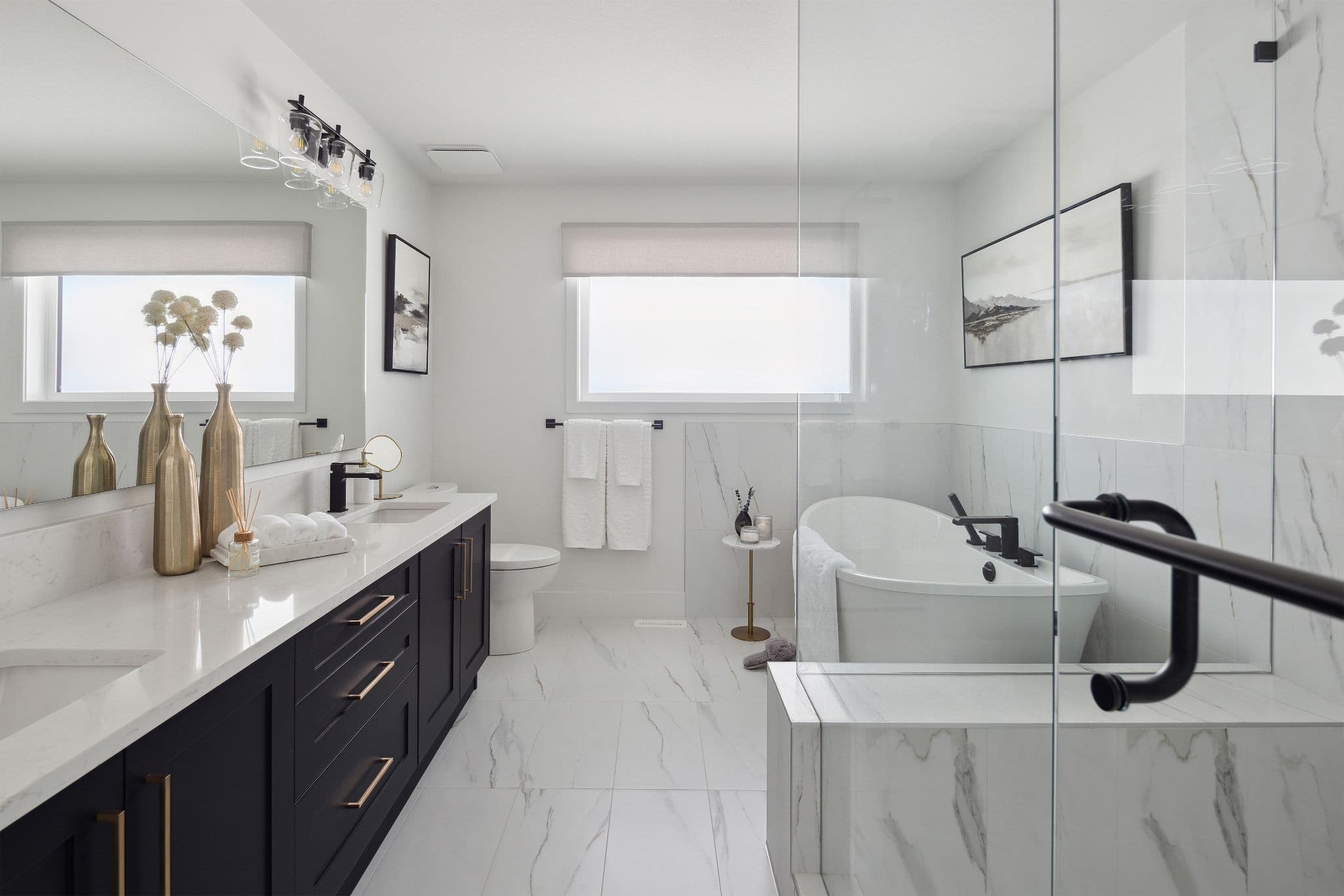 Timbers Edge – Primary bathroom with a freestanding soaker tub behind a glass partition, marble-look tile, and a navy double vanity with gold hardware.