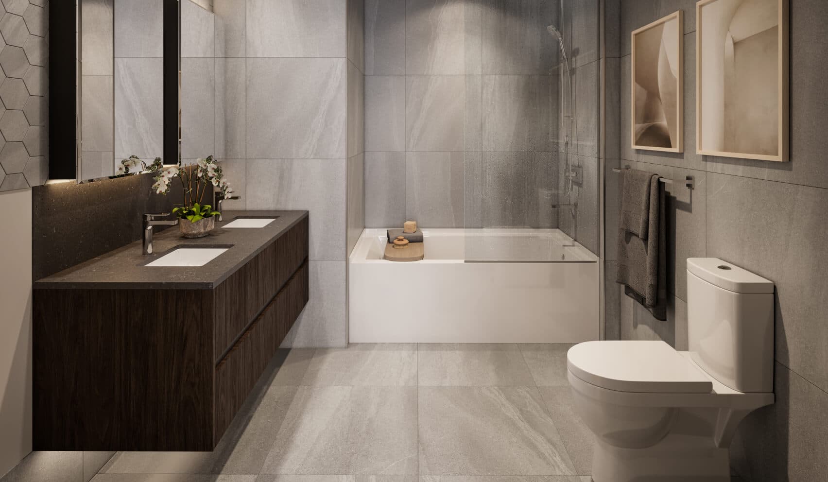 Fränk – A modern bathroom featuring large grey floor and wall tiles, a floating dark wood double vanity with a dark countertop, and a white bathtub with a glass divider screen. Soft under-cabinet lighting and muted earth tones create a serene, spa-like atmosphere.